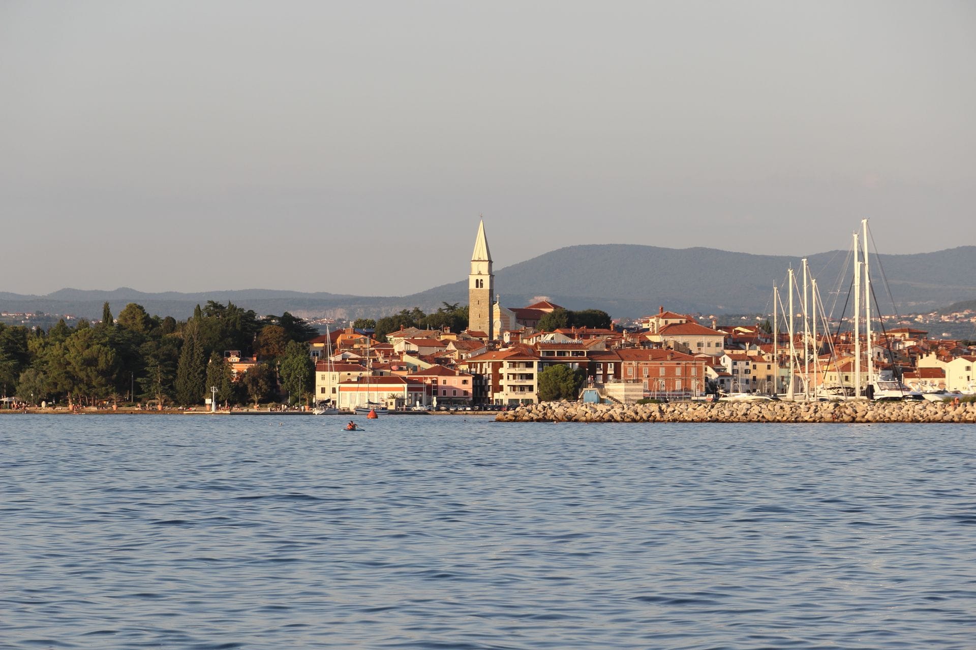 View of Izola, Slovenia from the sea, with St Mauro's church bell tower rising above the old town and sailboats moored in the marina